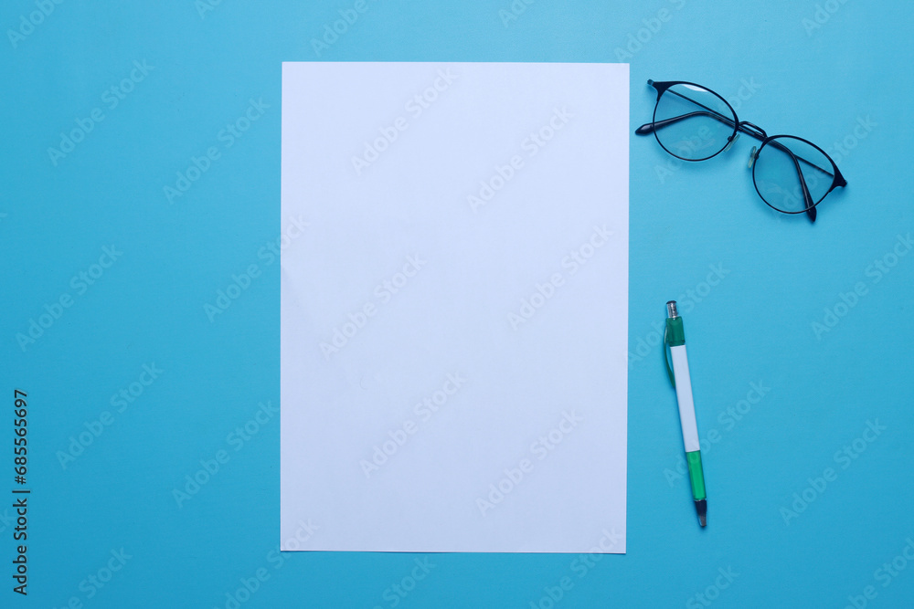Top view of white blank paper for mockup with eyeglasses and pen over blue background Top view of white blank paper for mockup with eyeglasses and pen over blue background