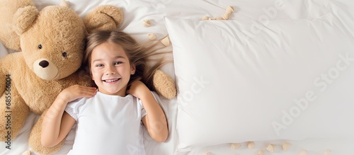 Top down view of a happy girl with a stuffed bear on a white pillow copy space image
