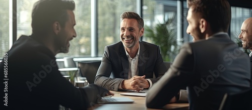 Two good looking businessmen are happily discussing a project in a conference hall One shares ideas with enthusiasm and the other listens attentively They sit at a desk and smile copy space image photo