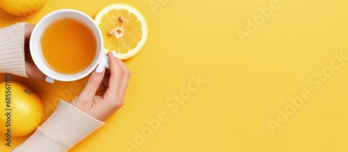 Top view photo of hands in yellow sweater holding cup of tea with lemon and smartphone on light orange background copy space image