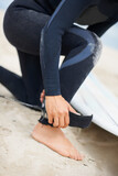 Foot, ankle and strap with a surfer on the beach closeup, getting ready for sports or fitness training. Hands, hobby and tie with a person on the sand at the coast for safety during an exercise hobby