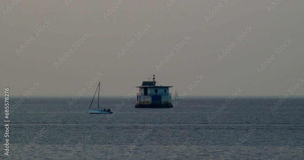 Two sailing boats float on the surface of the water at sunset, a lighthouse in the middle of the water Two sailing boats float on the surface of the water at sunset, a lighthouse in the middle of the water