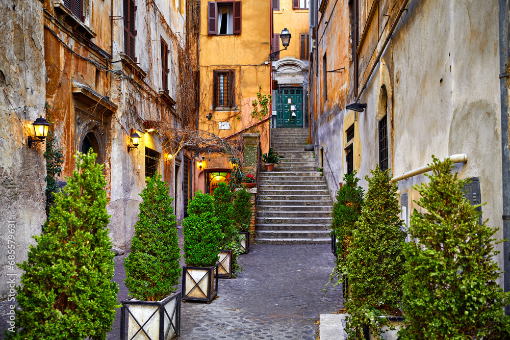 Rome, Italy. Yard of old street in downtown with antique building and stone stairs. Evening cityscape lamps on walls decorative plants flowerpots