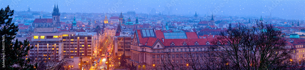 Prague Czech Republic. Wide panorama. Panoramic view at nighttime winter old town with falling snow, towers of prague. Illuminated street aerial Christmas time during seasonal holidays.