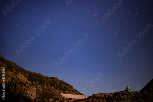 Night landscape with an alpine refuge and starry sky seen from rocky mountains