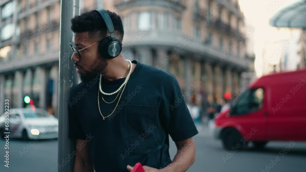 Pensive man with headphones in city, holding phone, urban soundscape and technology blend. Stylish millennial male enjoy listening to music in earphones in evening street outdoors. Slow motion Pensive man with headphones in city, holding phone, urban soundscape and technology blend. Stylish millennial male enjoy listening to music in earphones in evening street outdoors. Slow motion
