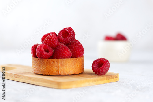 Tartlet with raw raspberries and cream, fresh dessert for breakfast on a wooden board.