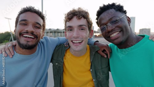Portrait of three young diverse male friends laughing at camera outdoors. Multiracial men friends having fun together enjoying life moments at city street. Youth community and friendship concept. photo