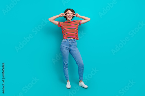 Full length photo of good mood adorable girl wear trendy outfit have fun demonstrate v-sign isolated on cyan color background