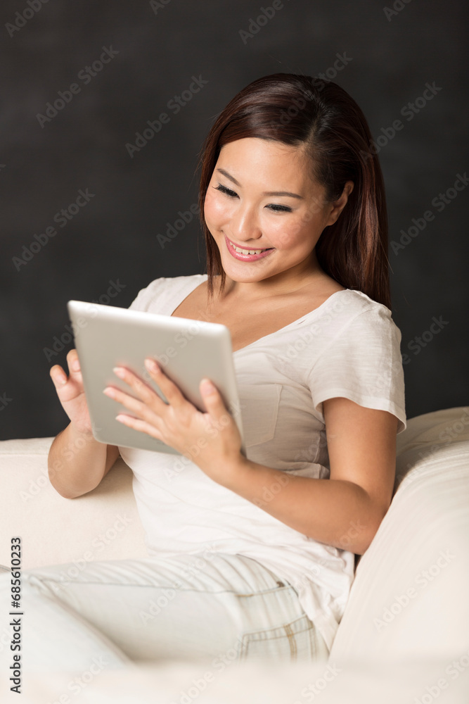 Chinese woman sitting on sofa using Digital Tablet Chinese woman sitting on sofa using Digital Tablet