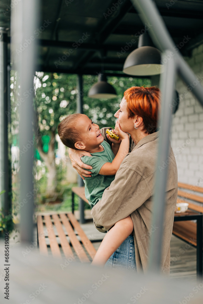 Family mother with her son holding on her hands playful mommy love enjoy time at the terrace redhead woman with short haircut