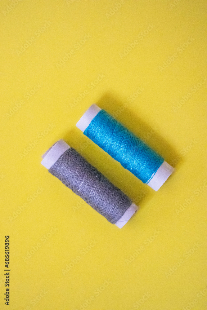 Sewing thread spool, isolated on yellow background. Colored threads are used by factories in the clothing industry. The thread is wound on a spool. Colored scrolls Sewing thread spool, isolated on yellow background. Colored threads are used by factories in the clothing industry. The thread is wound on a spool. Colored scrolls