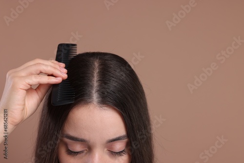 Woman with comb examining her hair and scalp on beige background, closeup. Space for text
