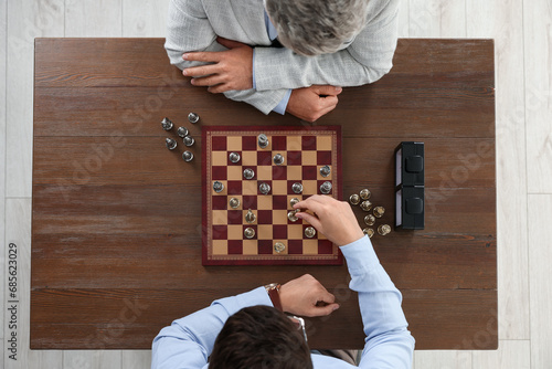 Men playing chess during tournament at wooden table, top view photo