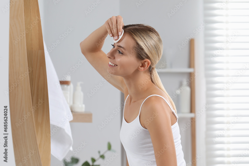 Smiling woman removing makeup with cotton pad in front of mirror in bathroom Smiling woman removing makeup with cotton pad in front of mirror in bathroom