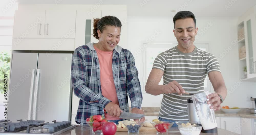 Happy diverse gay male couple preparing healthy fruit smoothie in kitchen, copy space, slow motion Happy diverse gay male couple preparing healthy fruit smoothie in kitchen, copy space, slow motion