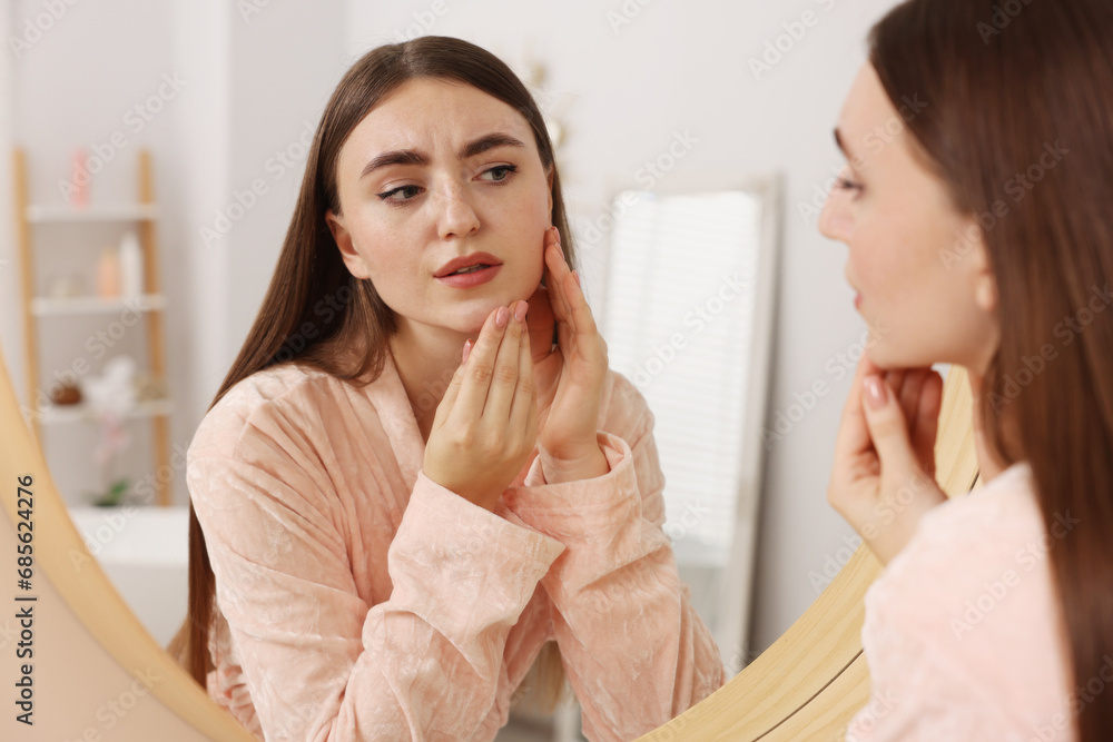 Young woman with skin problem looking at mirror indoors Young woman with skin problem looking at mirror indoors