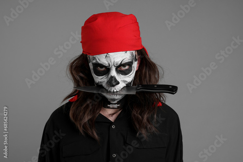 Man in scary pirate costume with skull makeup and knife on light grey background. Halloween celebration