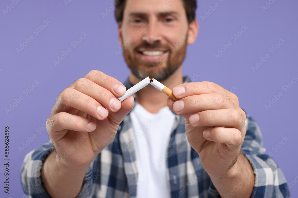 Stop smoking concept. Happy man breaking cigarette on purple background, selective focus Stop smoking concept. Happy man breaking cigarette on purple background, selective focus