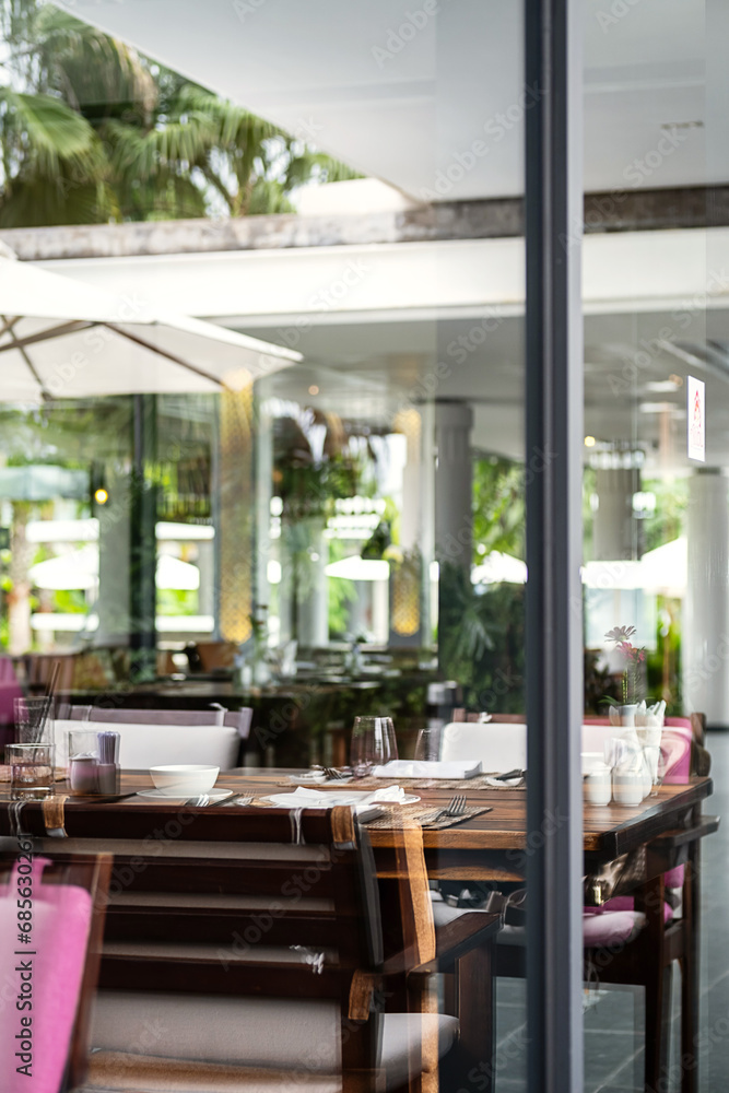 Fototapeta premium Hotel restaurant space with tables set for dinner at luxury resort, view through by window.