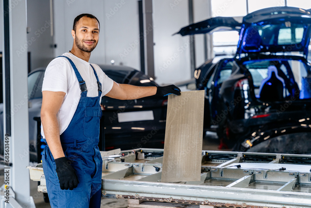 Handsome arabian mechanic man repairing electric car battery in workshop. Disassembling the battery of an electric vehicle engine.