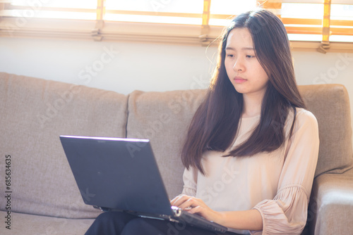 Business asian casual woman typing on laptop sitting on sofa in cozy home office