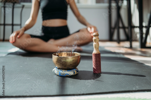 Incense burning in rin gong with woman exercising on mat in background photo