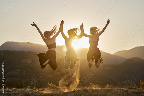 Cheerful friends holding hands and jumping at sunset photo