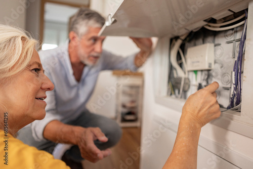 Woman examining electrical cable in fuse box with man at home photo