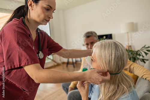 Doctor helping patient wearing oxygen mask at home photo