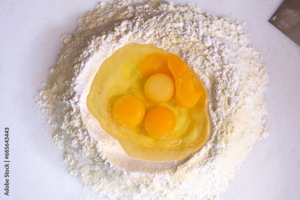 Flour and eggs ready for mixing. White flour and eggs on marble countertop.