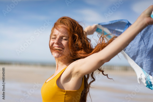 Cheerful woman with tousled hair playing with scarf on beach holiday photo