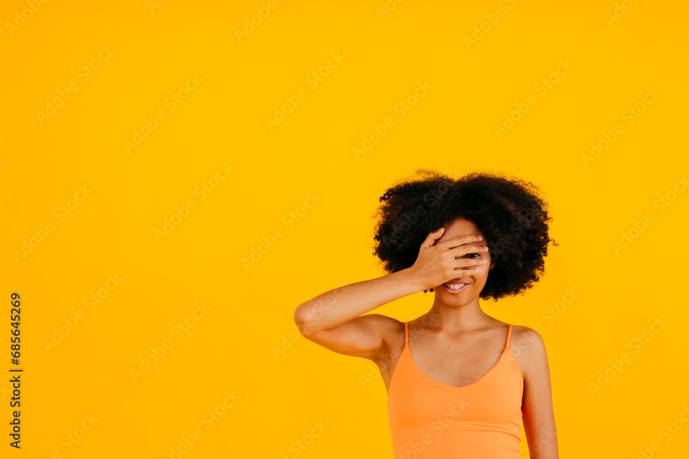 Smiling woman covering eyes against yellow background Smiling woman covering eyes against yellow background