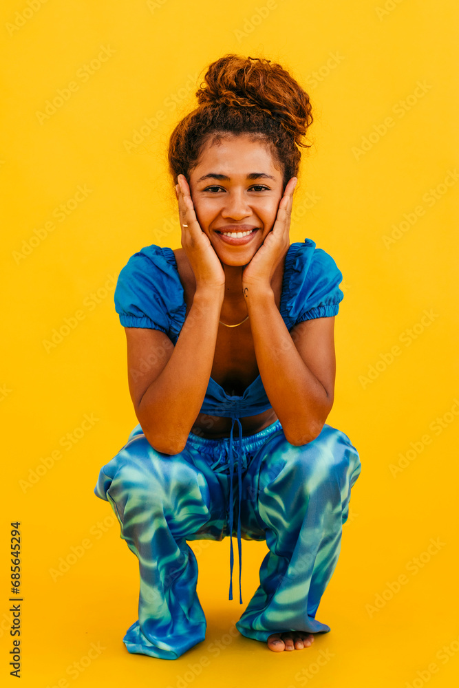 Smiling woman touching face crouching against yellow background Smiling woman touching face crouching against yellow background