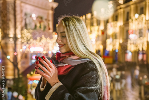 Happy woman with long hair holding cup of mulled wine at Christmas market photo
