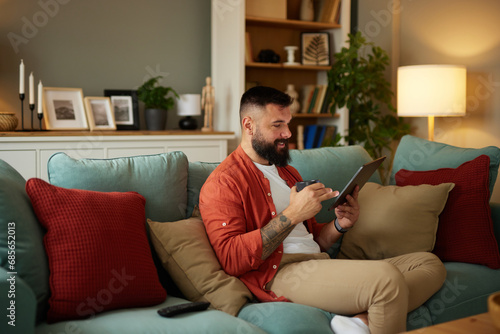 Tattooed man sitting on sofa using digital tablet at home
