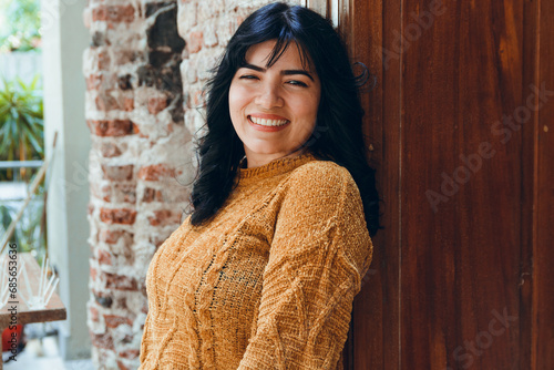 waist up portrait, young pretty latin woman smiling happy watching camera posing next to wooden door photo