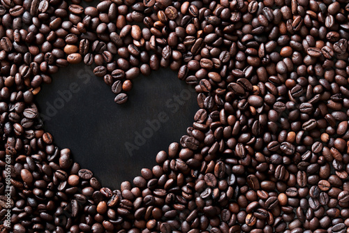 Coffee beans are laid out in the shape of a heart on a dark wooden surface. Top view. Roasted coffee beans  copy space