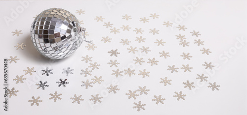 The disco ball lies on a white background strewn with silver snowflakes. New Year and Christmas background banner