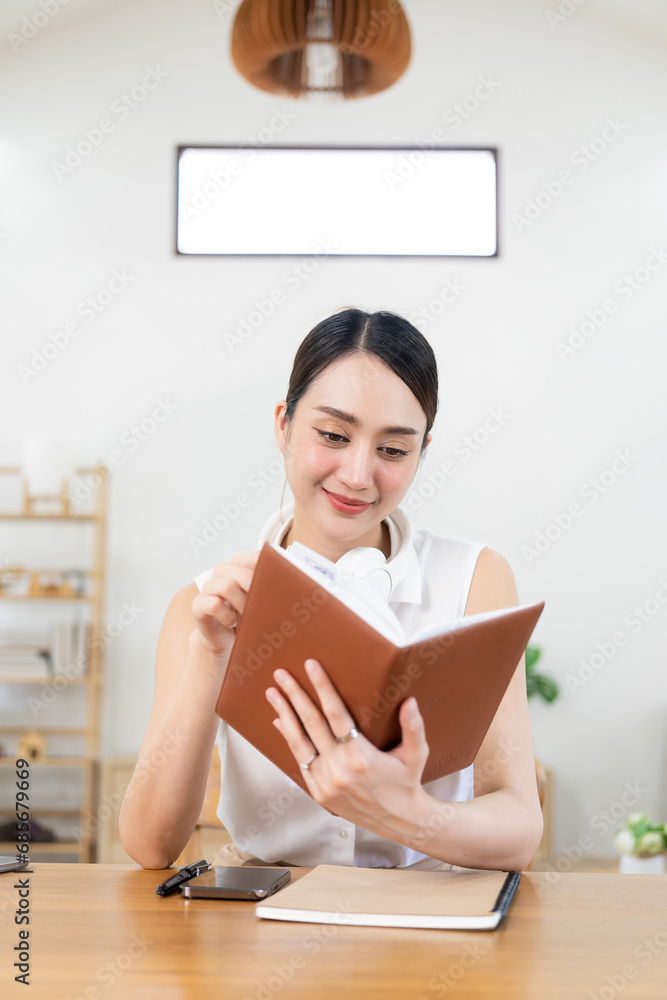 Attractive young Asian woman sitting in small living room enjoying reading a book, university school education college concept. Attractive young Asian woman sitting in small living room enjoying reading a book, university school education college concept.