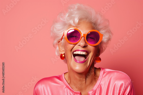 Happy senior woman in pink eyeglasses and hat on orange background