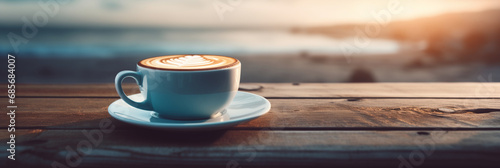 Blue coffee cup with latte art on dark rustic wood, seaside sunrice on backdrop. Image for mood board, poster,  aesthetic backdrop banner with copy space photo