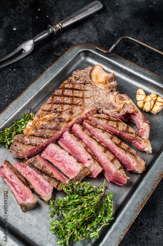Medium rare Grilled T-Bone Steak,  Florentine steak  sliced in a steel tray. Black background. Top view