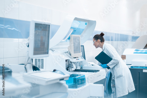 A laboratory technician in a lab coat performs a series of tests on a chemical analyzer in a bio laboratory. impersonal unrecognizable laboratory blurred fuzzy background shot through glass with space