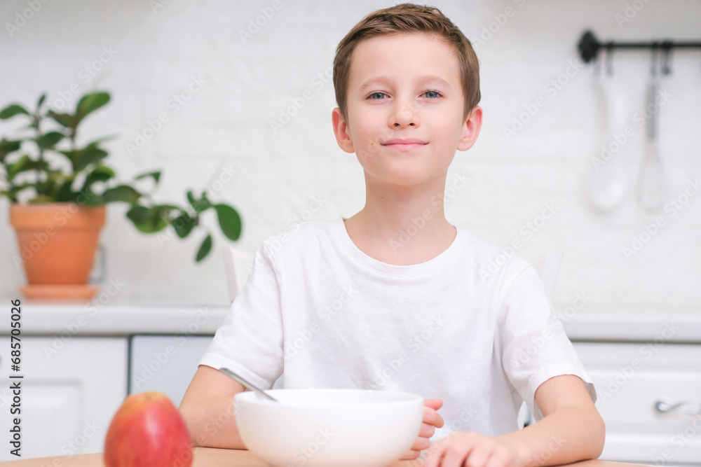 Little boy eating cereal with milk, apple for breakfast at wooden table in light white kitchen. Little boy eating cereal with milk, apple for breakfast at wooden table in light white kitchen.