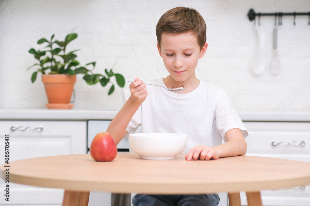 Little boy eating cereal with milk, apple for breakfast at wooden table in light white kitchen. Little boy eating cereal with milk, apple for breakfast at wooden table in light white kitchen.