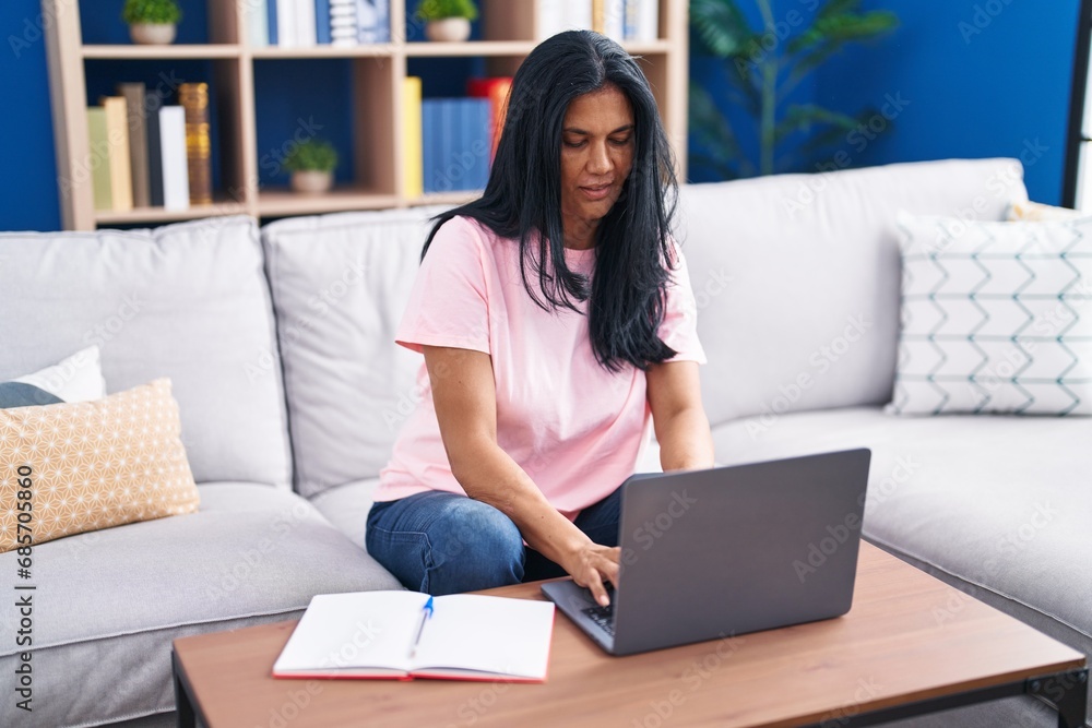 Middle age hispanic woman using laptop sitting on sofa at home Middle age hispanic woman using laptop sitting on sofa at home