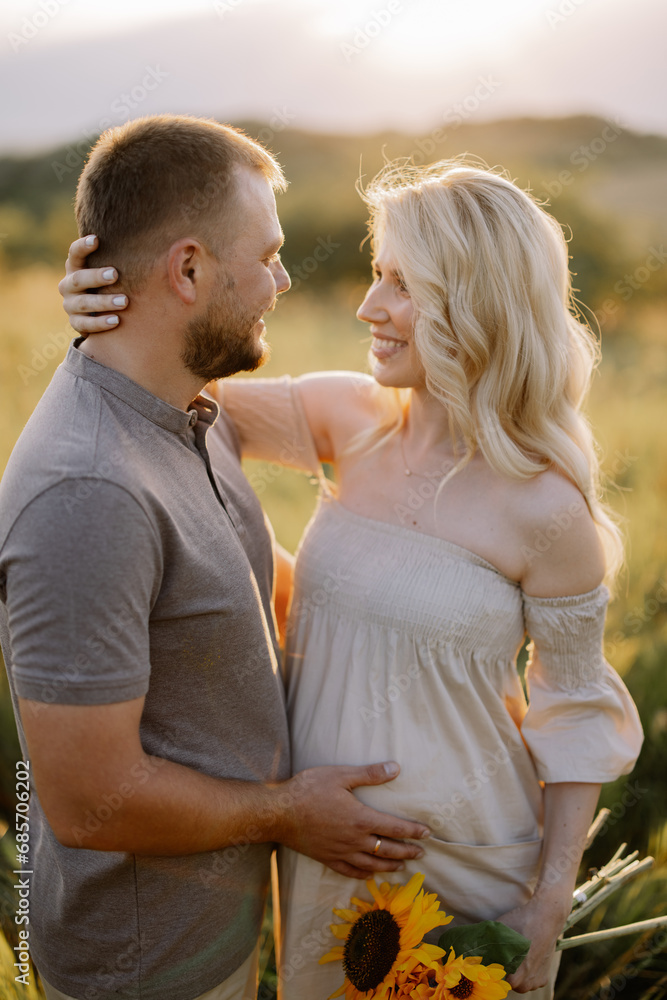 Happy and in love pregnant couple with a bouquet of sunflowers spending time together outdoors at sunset. Happy and in love pregnant couple with a bouquet of sunflowers spending time together outdoors at sunset.