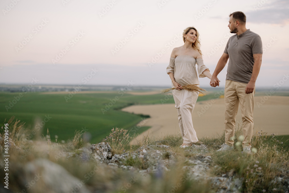 Portrait of a happy pregnant couple with a bouquet of sunflowers spending time together walking in the mountains at sunset Portrait of a happy pregnant couple with a bouquet of sunflowers spending time together walking in the mountains at sunset