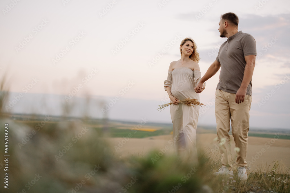 Portrait of a happy pregnant couple with a bouquet of sunflowers spending time together walking in the mountains at sunset Portrait of a happy pregnant couple with a bouquet of sunflowers spending time together walking in the mountains at sunset